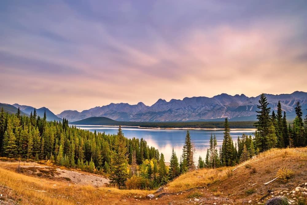 An awe-inspiring mountain range in Kananaskis, with a serene lake and towering trees in the background.