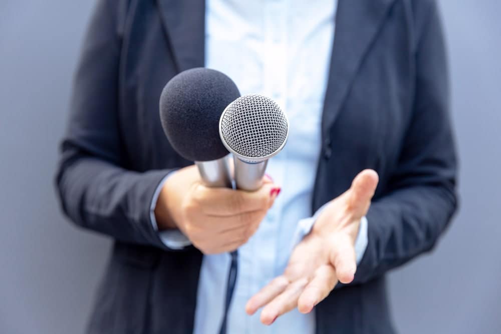 A woman is holding two microphones while providing public comment at an Oregon State Parks Dept meeting regarding increased out-of-state RV fees.