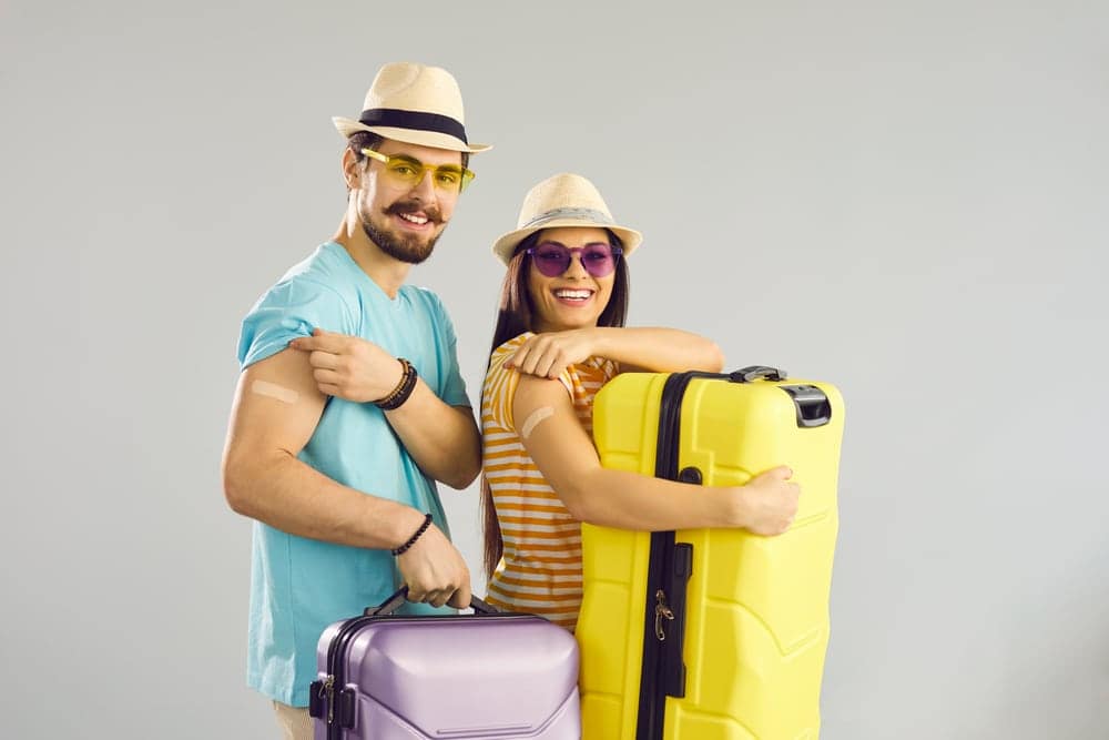 Young couple with suitcases posing on gray background, showcasing their excitement for their upcoming trip to Canada.