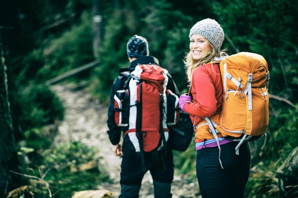 Two people with backpacks hiking down a trail in the woods.