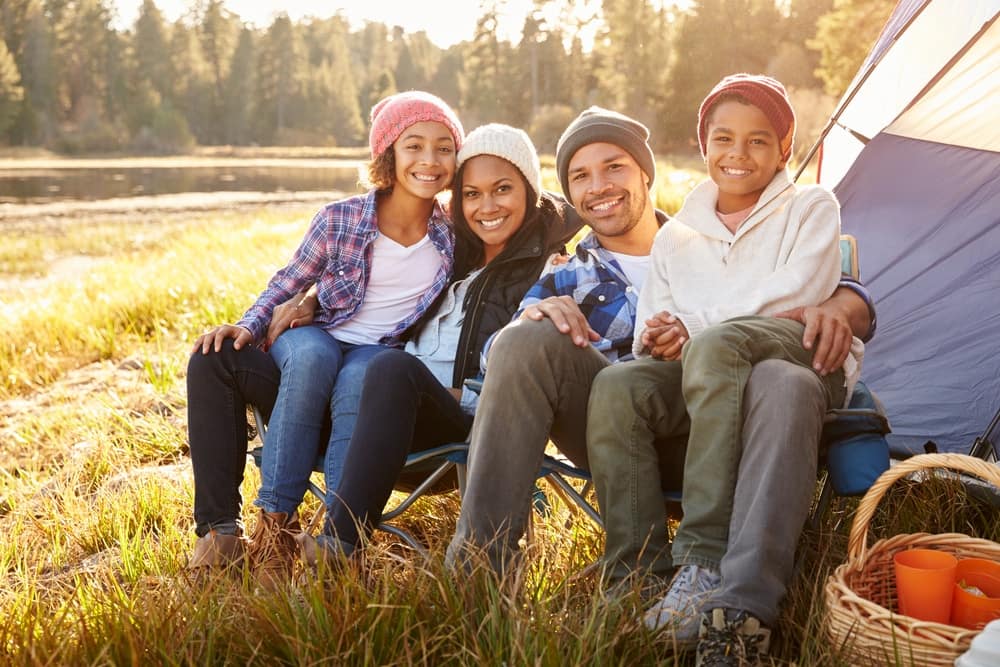 A Black family sitting in front of a tent, enjoying the outdoors during a camping trip.