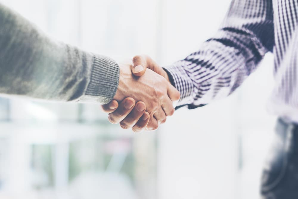 Two businessmen shaking hands during an outdoor media summit.