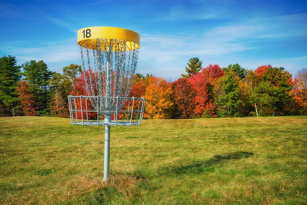 A yellow disc golf basket in a grassy field.
