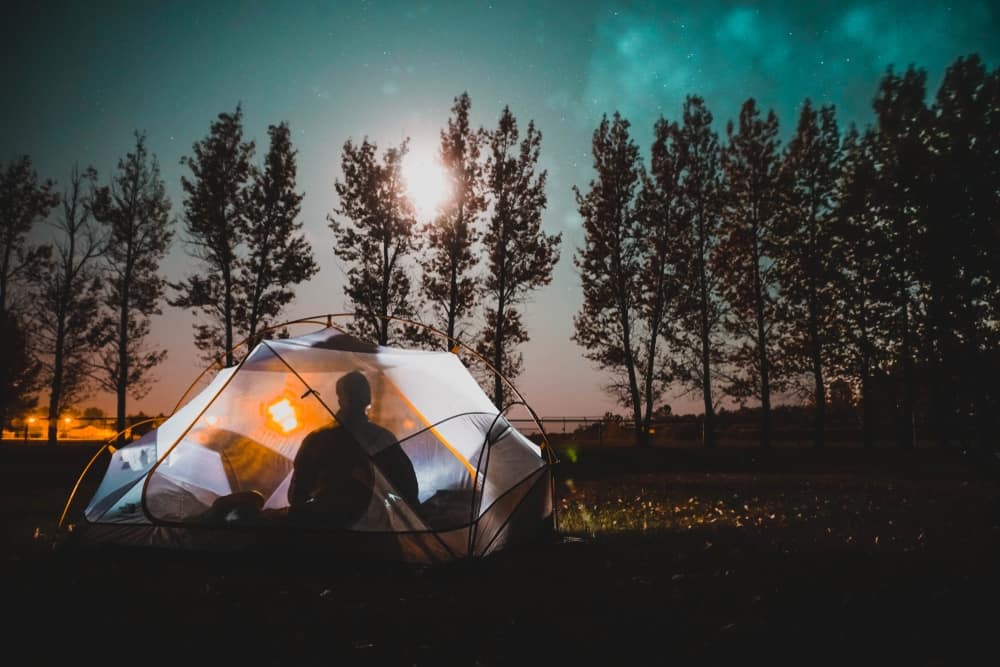 A person sits in a tent under a full moon while winter camping in Saskatchewan Parks.