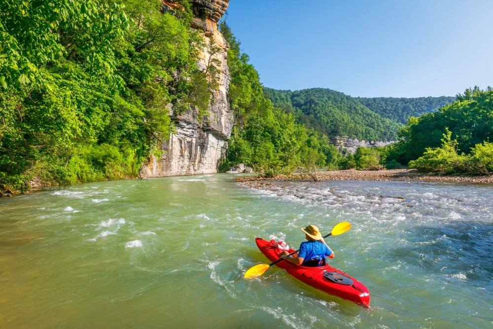 Director Katherine Andrews is kayaking down a river near a cliff.