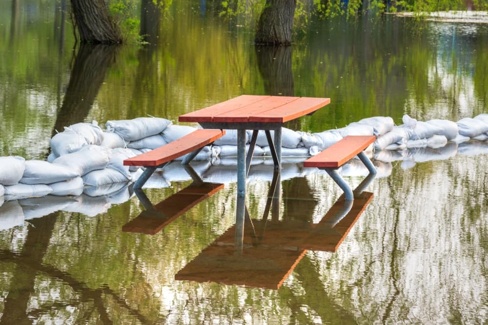 A picnic table sits on top of sandbags in a flooded area.