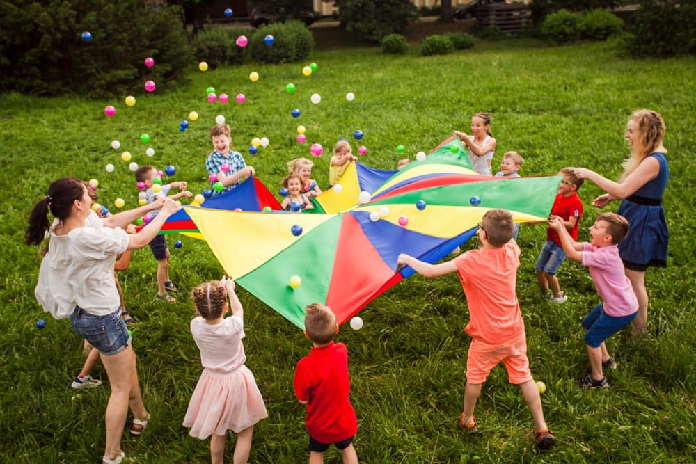 A group of children celebrates while playing with a colorful kite in a park.