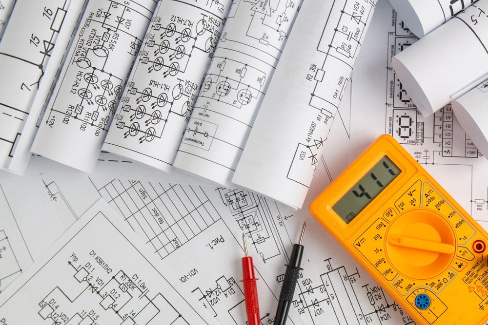 A magnifying glass and a multimeter on top of blueprints outlining an RV park in the municipality of Alaska.