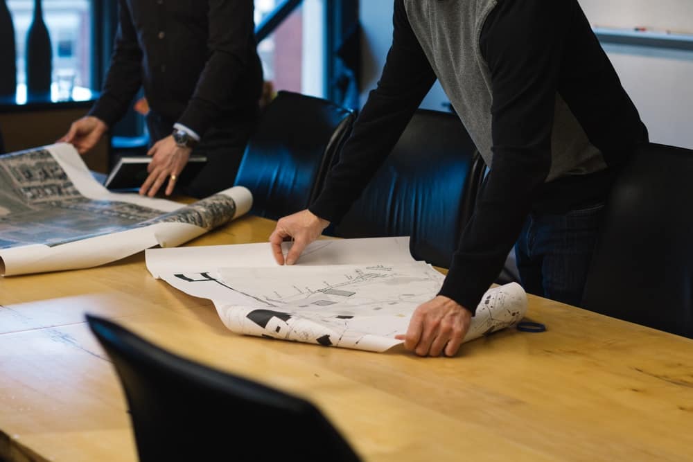 A group of people from the WA Shire standing around a table with paper on it, brainstorming facility upgrades to boost progress.
