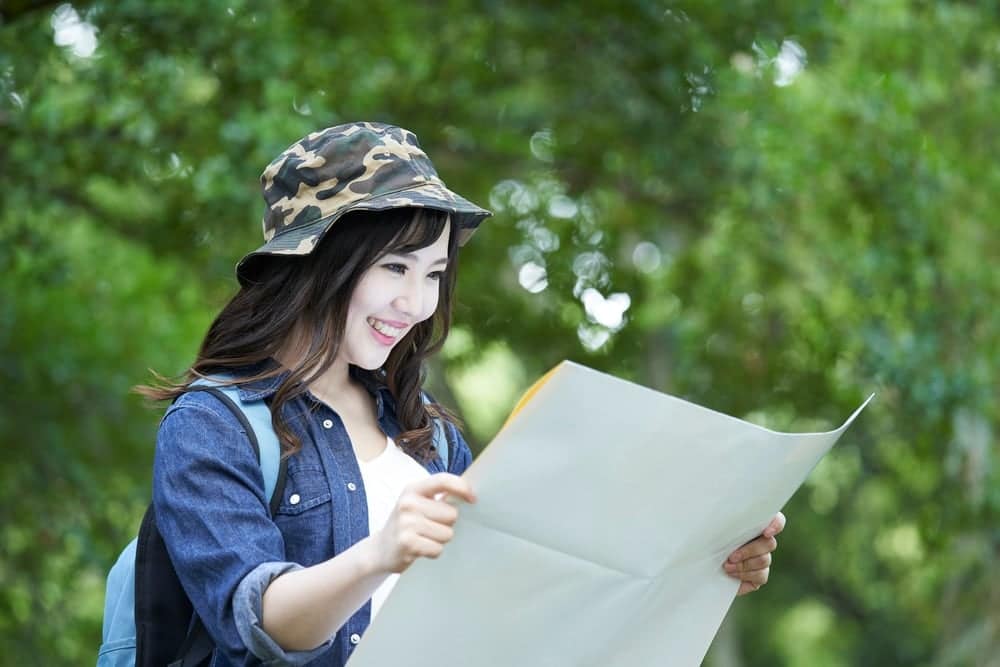 A young Asian woman holding a map at Snow Peak in the park.