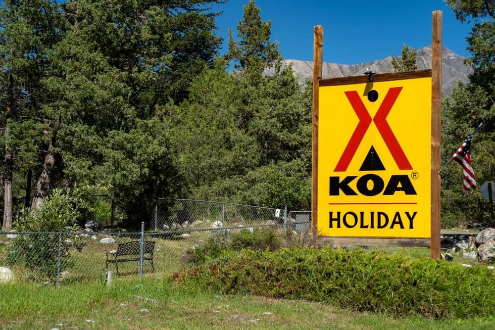 A sign promoting the KOA Annual Convention in front of a forest.