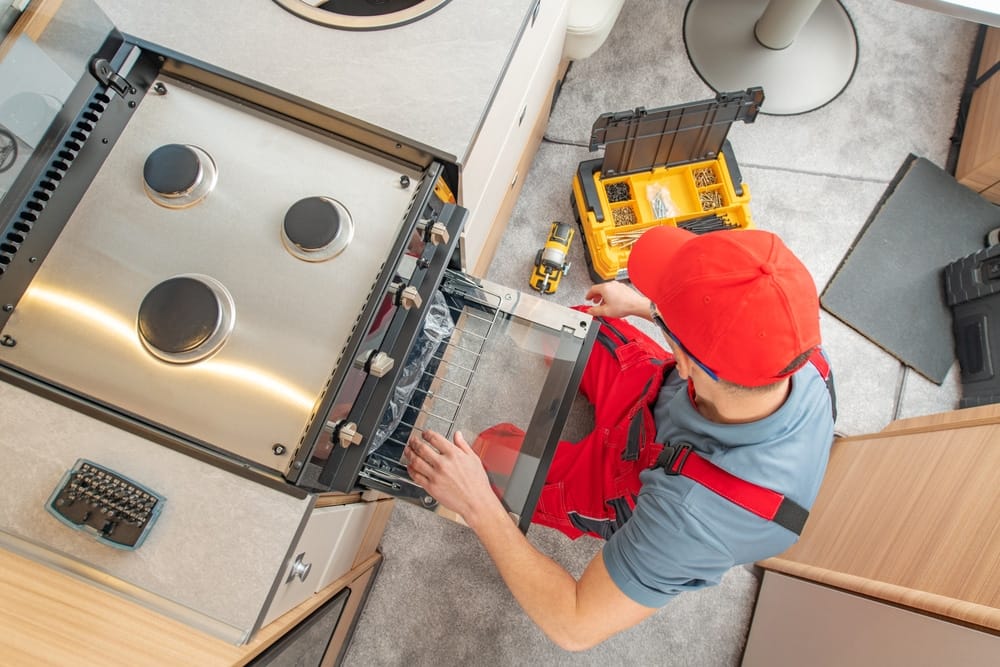A man is repairing an oven in a kitchen.
