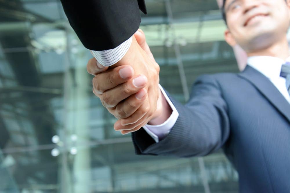 Two businessmen shaking hands in front of a glass building.