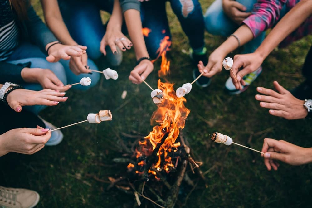 A group of friends gathered around a campfire roasting marshmallows, while MARVAC congratulates and KOA serves as the perfect location for their outdoor adventure.