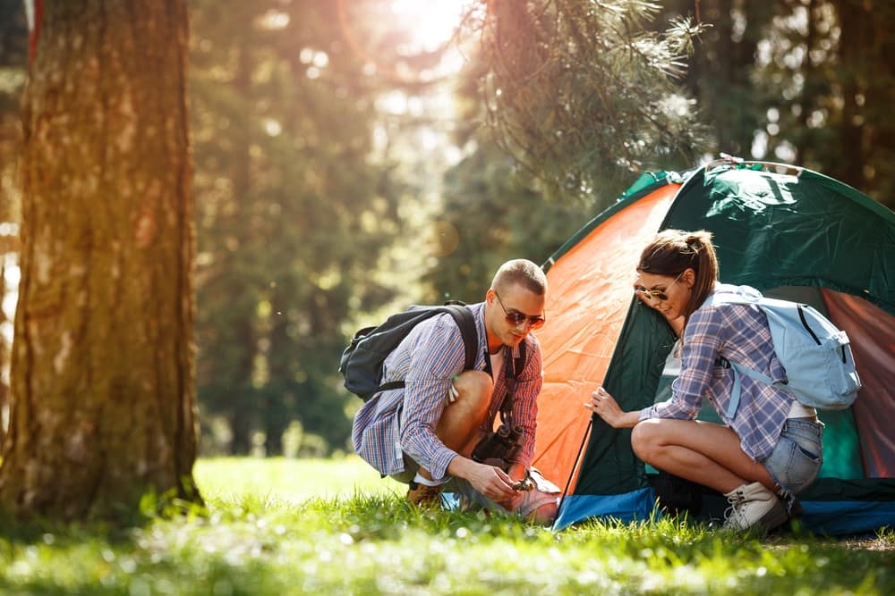 A man and woman enjoying outdoor recreation next to a tent in the woods.