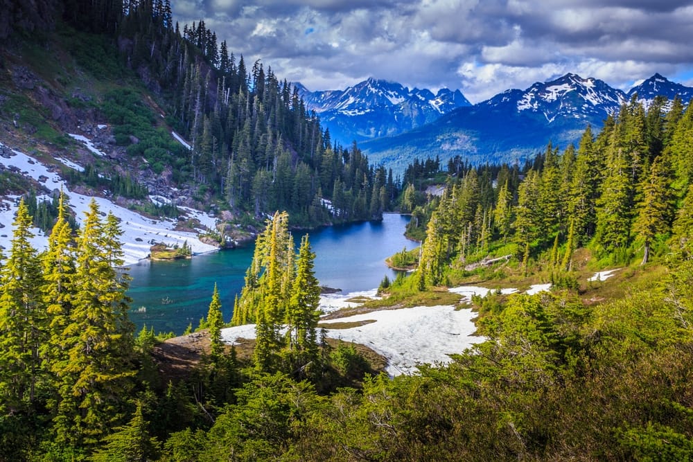 A scenic mountain lake nestled amidst towering trees and glistening snow, showcasing the natural beauty that can be preserved through National Park System protection.