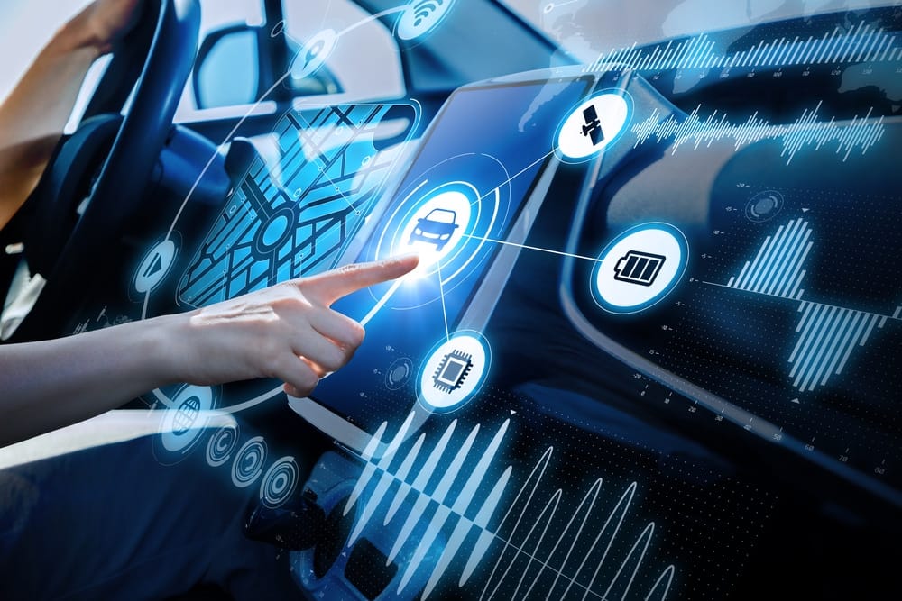 A person is pointing at a touchscreen in an EV car while considering an investment opportunity in the auto industry.