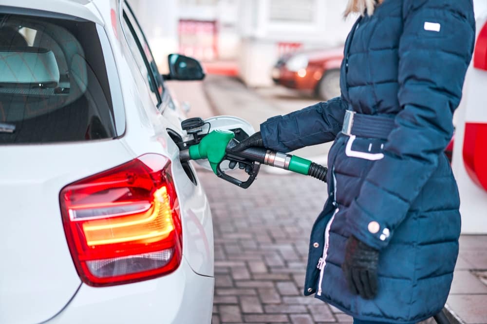 A woman is filling up her car at a gas station during the shorter days of the year.