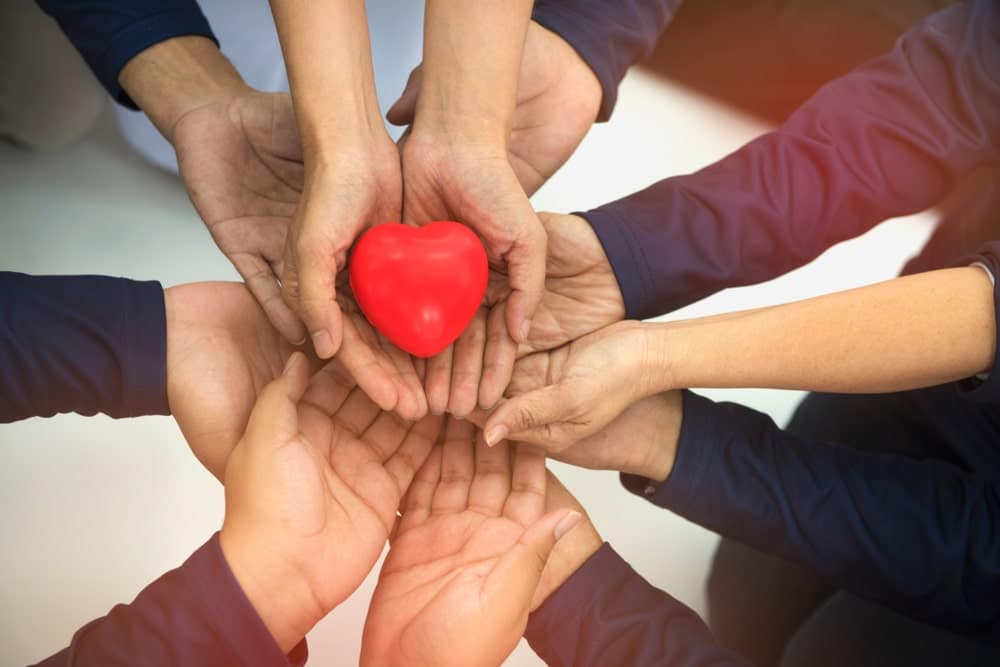 A group of people holding a red heart in their hands.