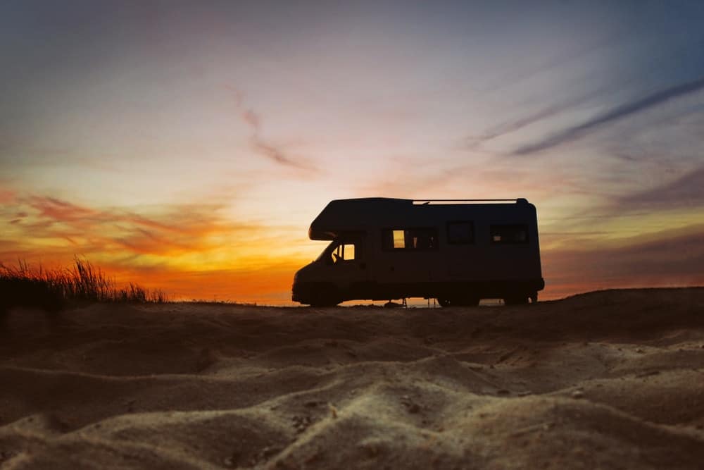 An rv sits in the sand at sunset.