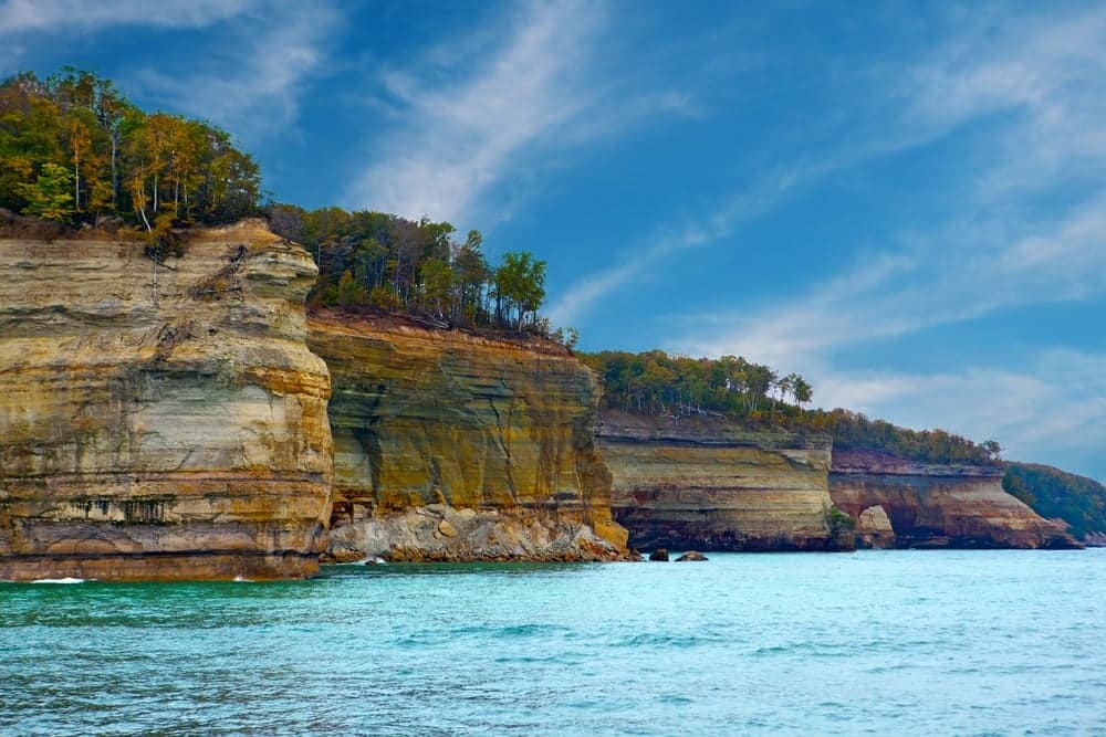 Pictured Rocks National Lakeshore features a breathtaking rocky shoreline adorned with majestic trees and towering cliffs.