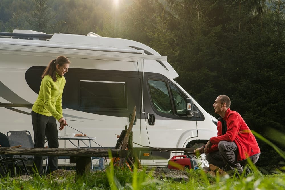 A man and woman standing next to an RV in the woods, showcasing the Go RVing experience.