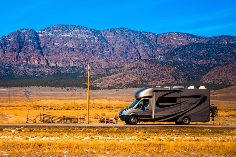 An RV, endorsed by the RVIA, triumphantly parked on a road with majestic mountains in the background. Through its presence, it acts as an advocate for adventurous journeys and outdoor exploration.