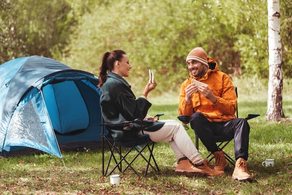 A man and woman sitting in chairs outside by a tent.