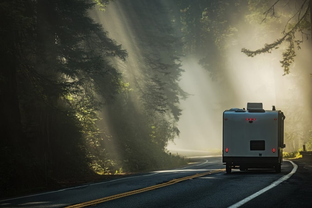 An RV, belonging to RVIA members, traveling down a road in California's forest.