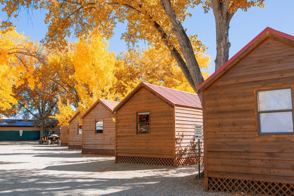 A row of wooden cabins with trees in the background, located in a campground.