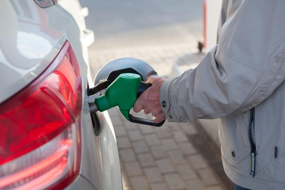 A man filling up his car with gas at lower prices, benefiting consumers.