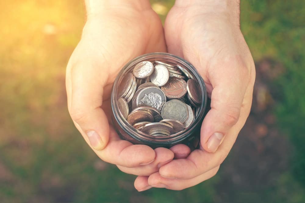 A man's hands holding a jar full of coins.