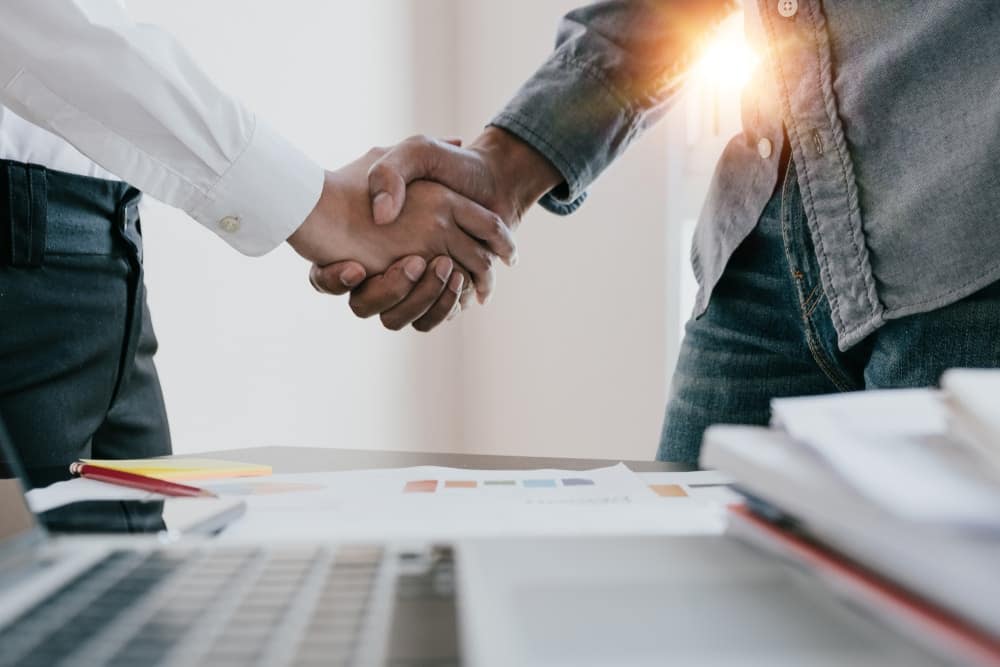 Two business people from Empowered Ventures and Paramount Plastics shaking hands in front of a desk.