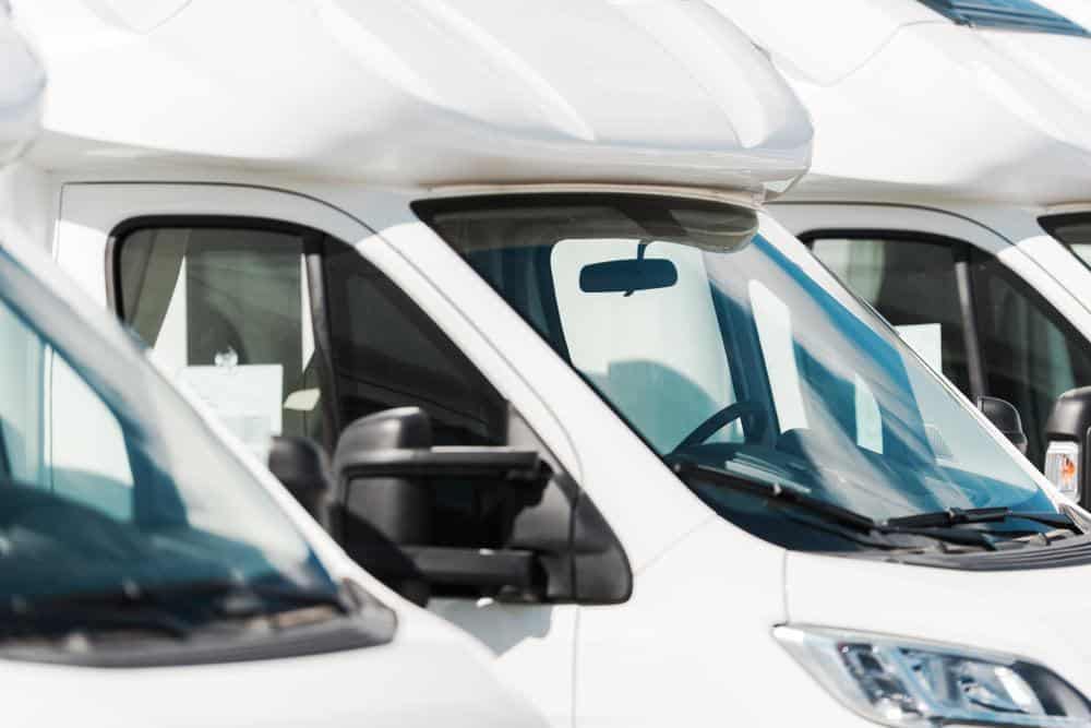 A row of white rvs in a parking lot.