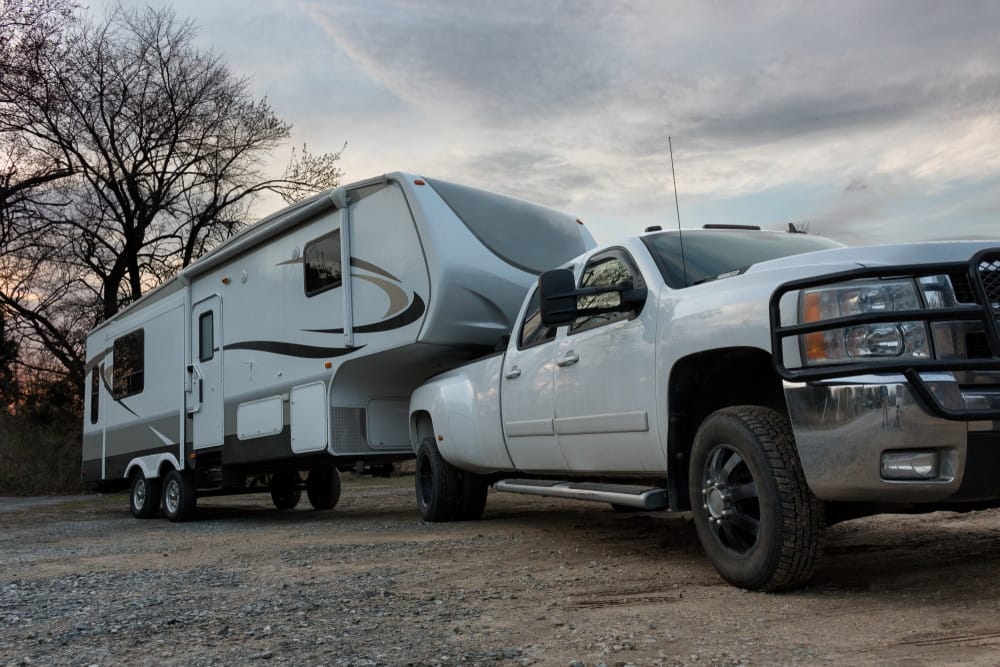 A white truck towing a fifth wheel RV.