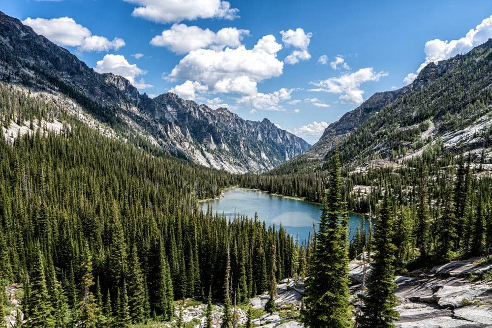 Rombo Campground nestled in a serene forest with majestic mountains and lush trees, offering a tranquil escape for all visitors. Public input welcome to enhance the natural beauty of this picturesque lake setting.