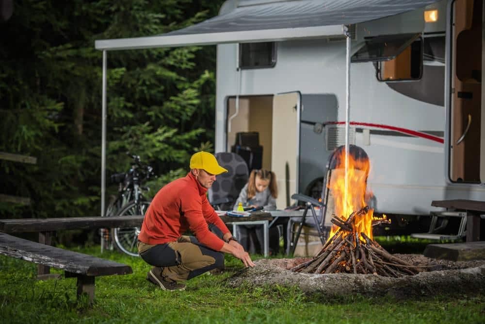 A family sits around a campfire in front of an RV, enjoying the coziness and warmth provided by their recreational vehicle.
