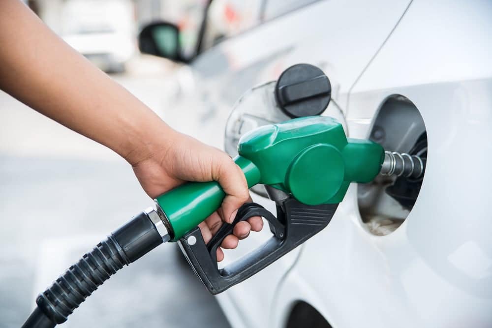 A person is filling up a car with gas, monitoring the fluctuating gas prices.