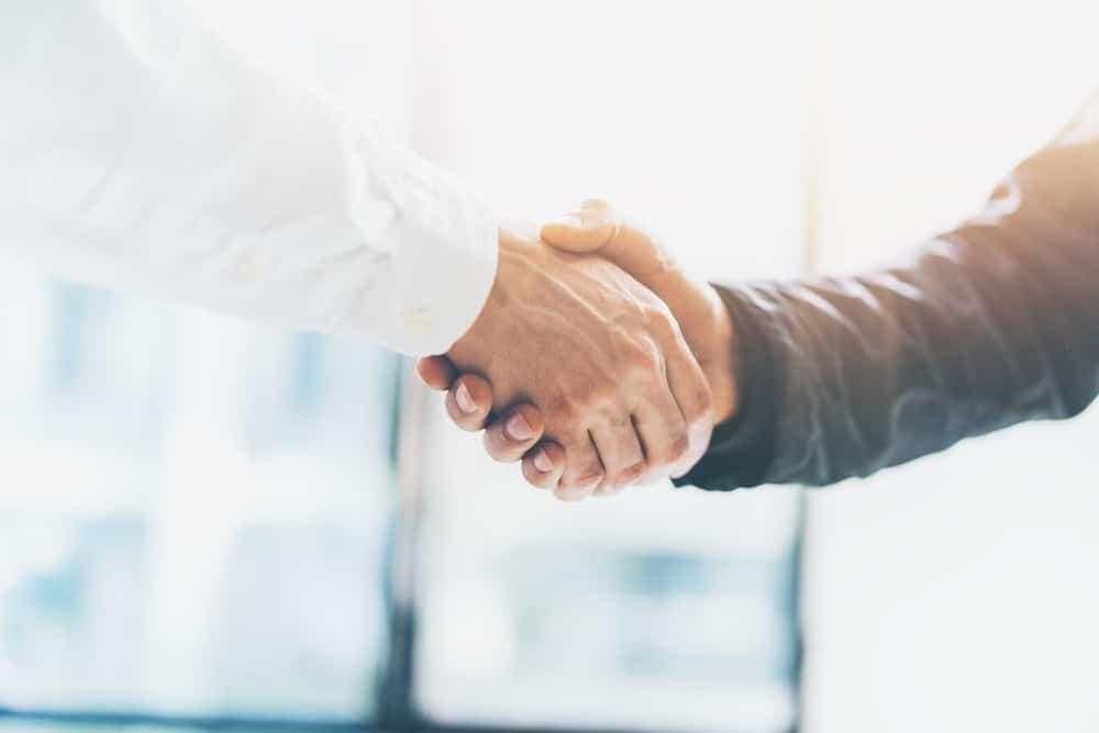 Two business people shaking hands in front of a window at Technexus Venture Collaborative.