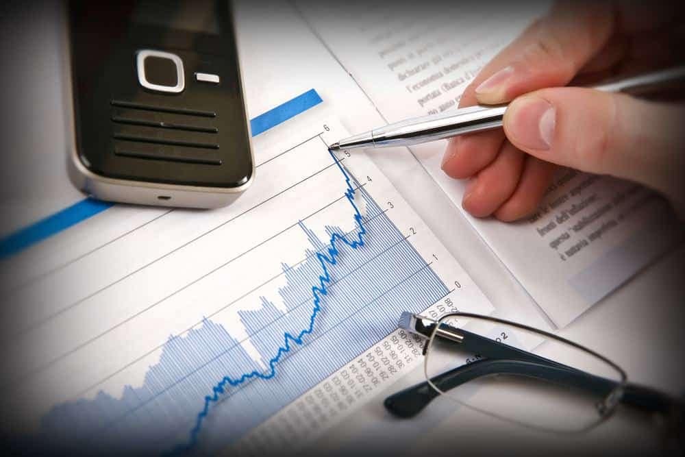 A person is holding a cell phone and writing on a graph while participating in a conference call.