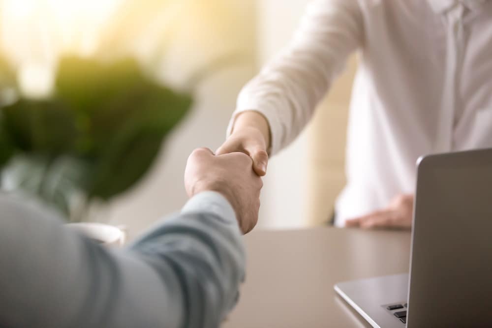 Gregory Katt, from the Marshall & Sterling Insurance team, shaking hands with a member of the Campground & RV Park Sales Team in front of a laptop.
