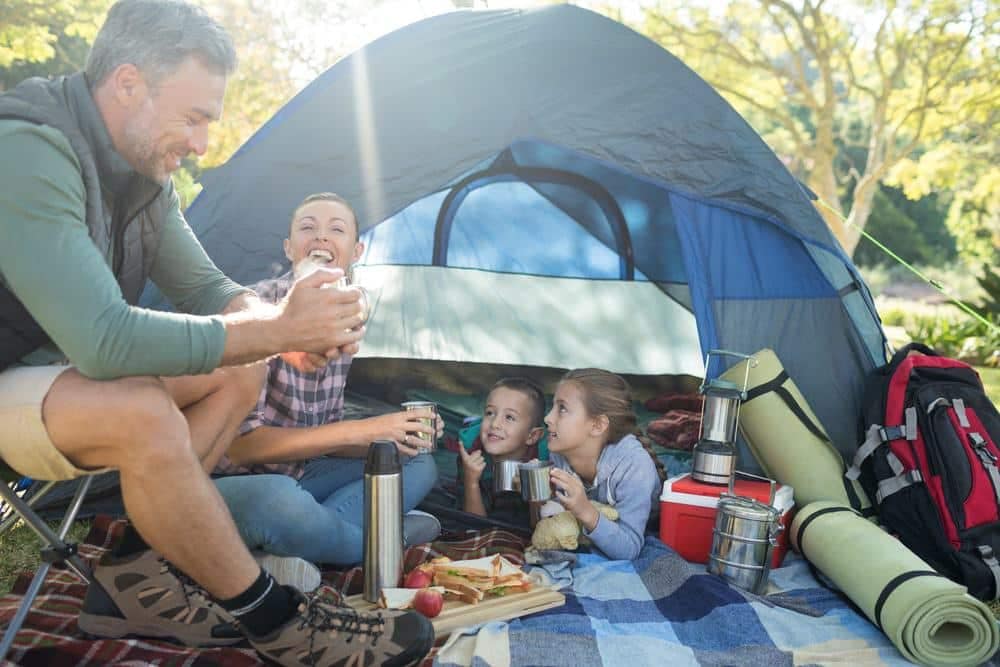 A family is enjoying a picnic in front of their tent.