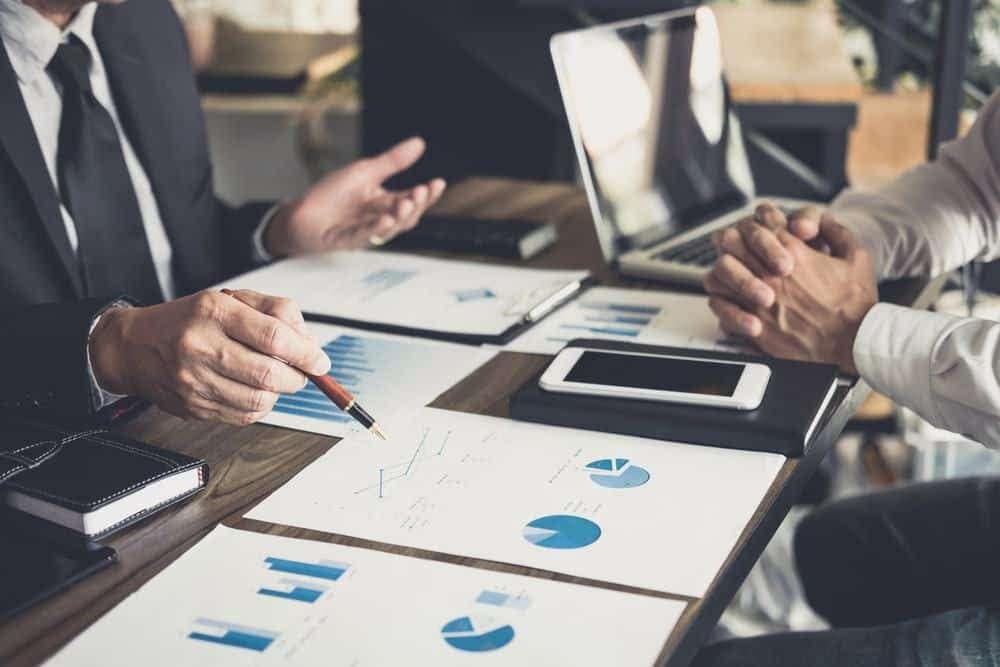 Two businessmen talking at a table with graphs.