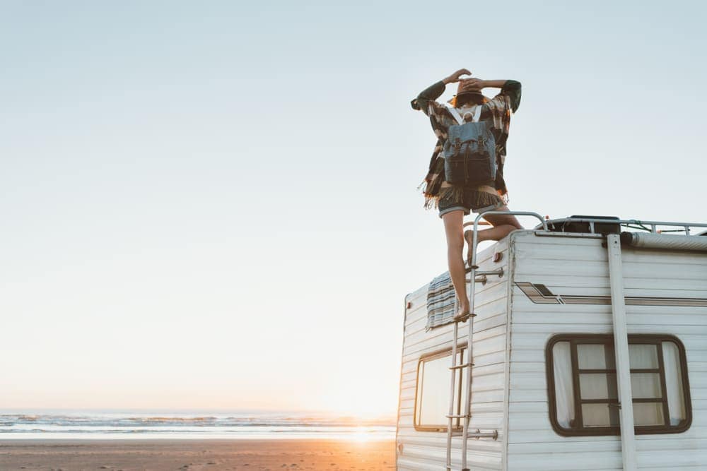 A woman standing on top of a Delmarva RV Sales camper on the beach.