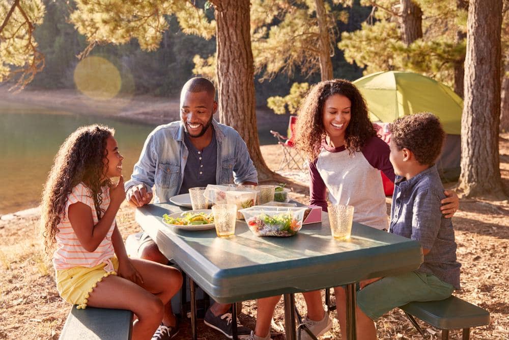 A family camps at a picnic table in the woods.