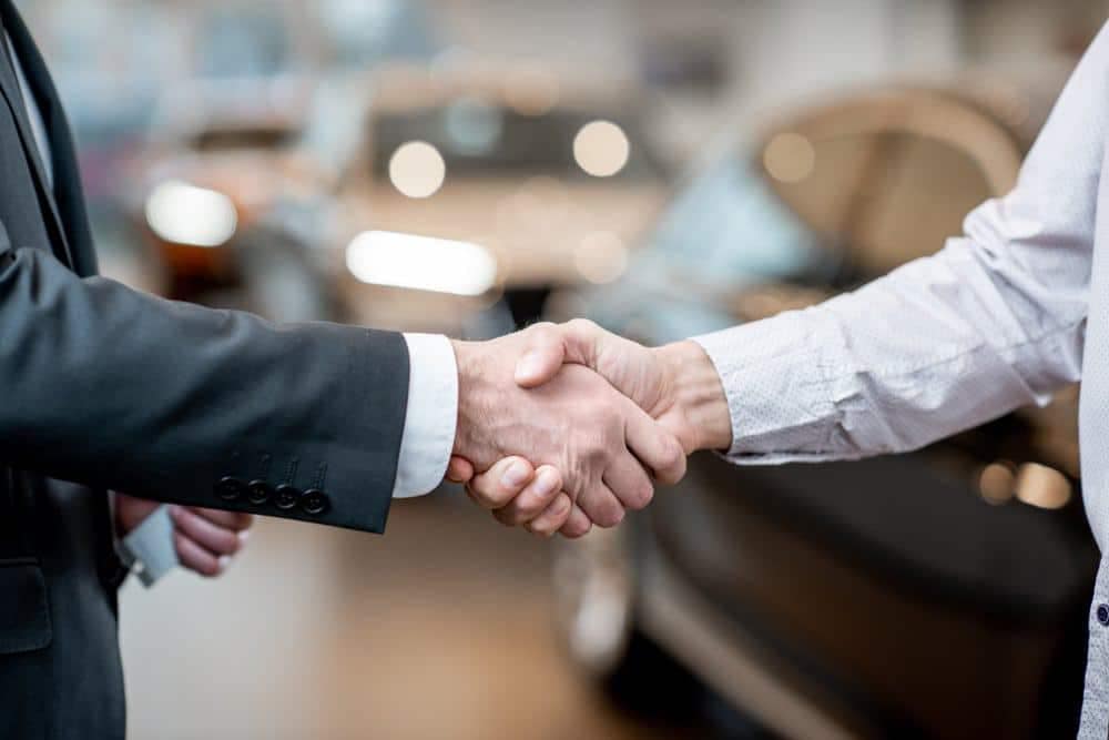 Two men shaking hands in front of a Midwest Outdoor Resorts dealership.