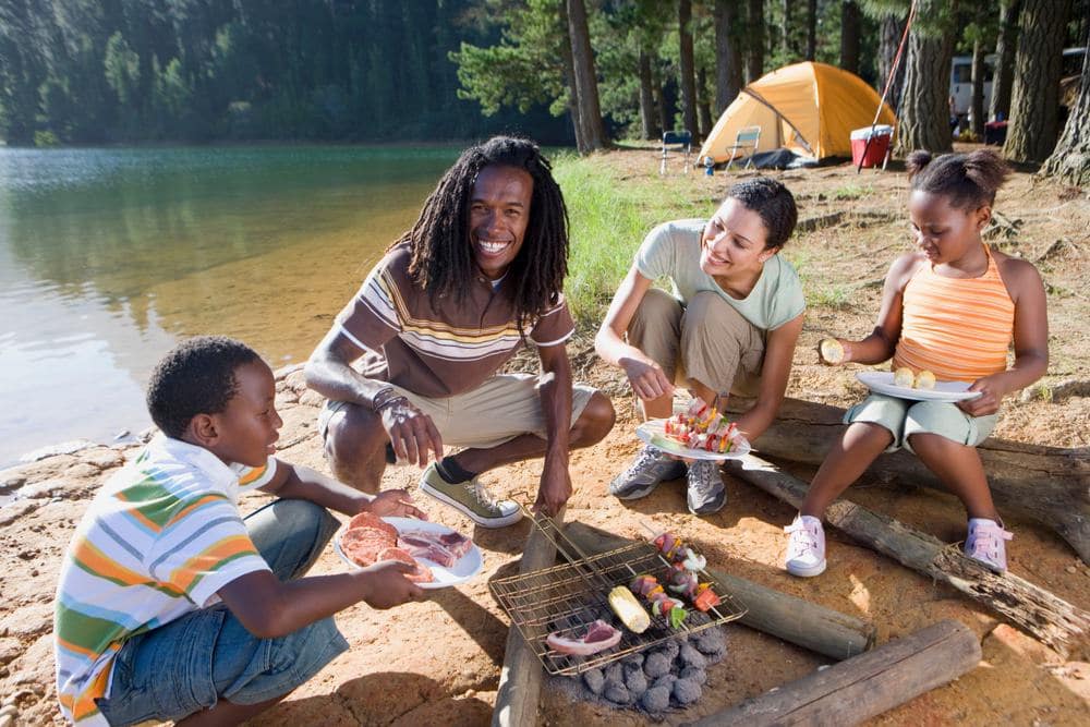A group of people sitting around a campfire near a lake during a holiday.