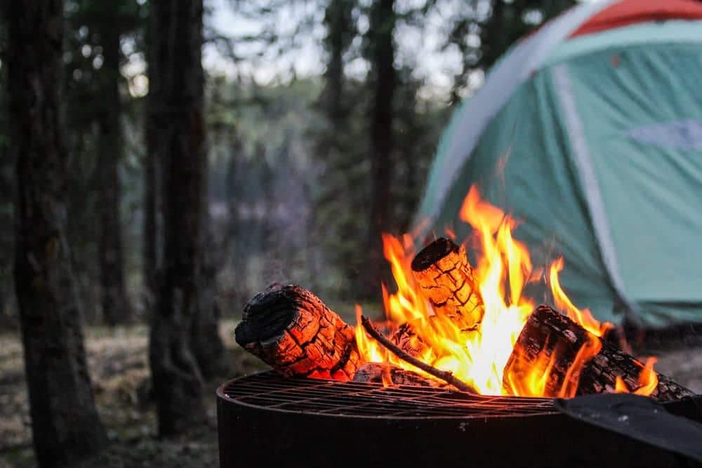 A campfire in the woods with a tent in the background.