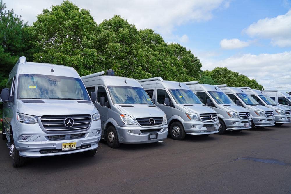 A row of silver mercedes benz rvs parked in a parking lot.