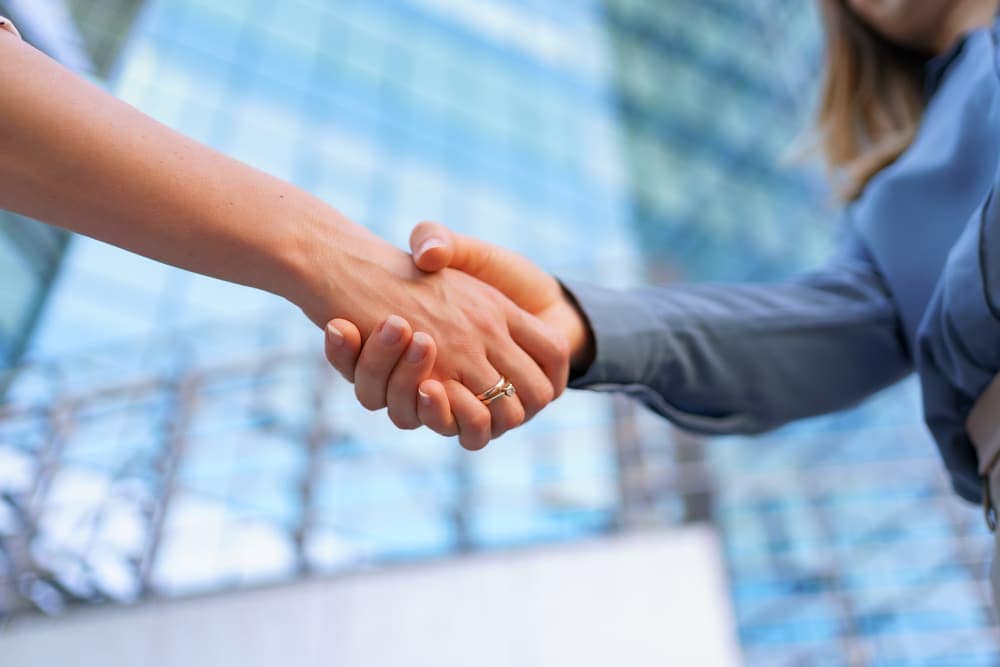 Two business people shaking hands in front of a building.